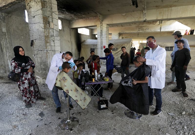 &copy; Reuters. Volunteer hairdressers cut the hair of internally displaced children, amid concerns over the spread of the coronavirus disease (COVID-19), at an IDP camp in Idlib