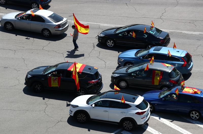 © Reuters. Un manifestante con mascarilla camina portando una bandera de España entre coches en Madrid