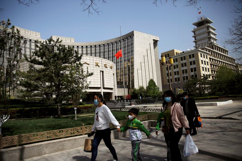 &copy; Reuters. FILE PHOTO: People wearing face masks walk past the headquarters of PBOC, where the Chinese national flag flies at half mast