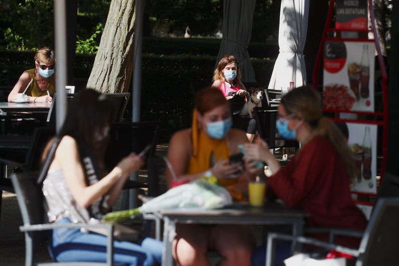 &copy; Reuters. Pessoas com máscara de proteção sentam em mesas de quiosque no Parque del Retiro, em Madri