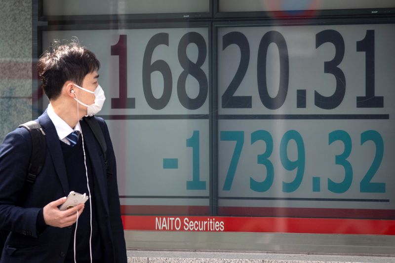 &copy; Reuters. A man wearing a protective face mask walks past a screen showing Nikkei index in Tokyo