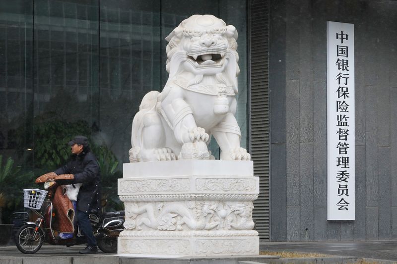 © Reuters. A man rides an electric bike past the CBIRC building in Beijing