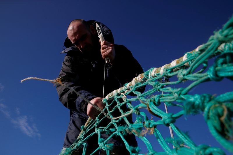 © Reuters. FILE PHOTO: A fisherman repairs a fishing net on the dock of the port in Boulogne-sur-Mer