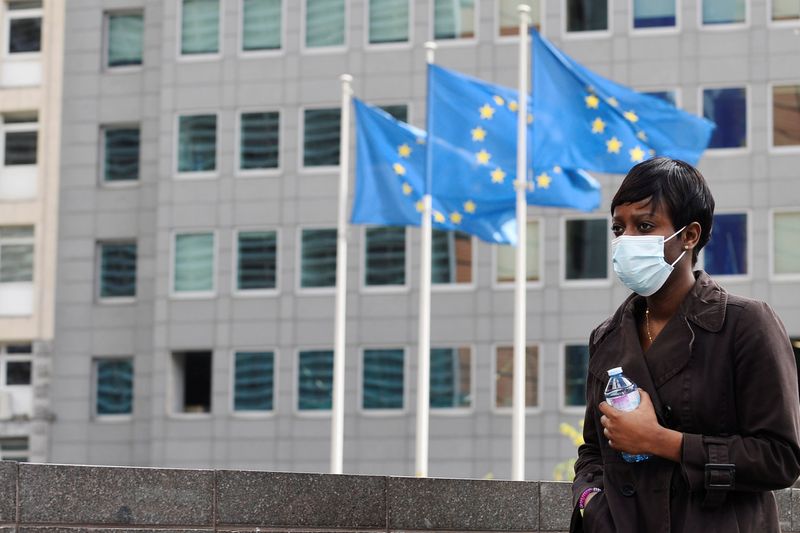 &copy; Reuters. Una donna con una maschera davanti alle bandiere della sede centrale della Commissione Europea a Bruxelles