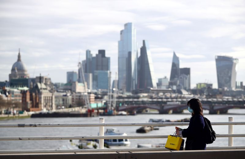 &copy; Reuters. A woman wearing a protective mask walks across Waterloo Bridge in front of the City of London financial district during rush hour, as the number of Coronavirus cases grow around the world, in London