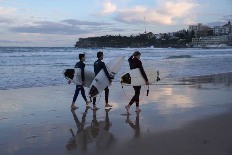 &copy; Reuters. Surfers walk along the water&apos;s edge at Bondi Beach in Sydney