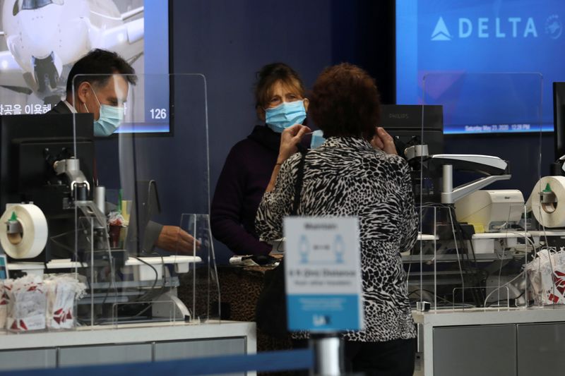 © Reuters. A customer puts on a protective face mask while talking with a Delta Air Lines, Inc. employee at Los Angeles International Airport (LAX) on an unusually empty Memorial Day weekend during the outbreak of the coronavirus disease (COVID-19) in Los Angeles