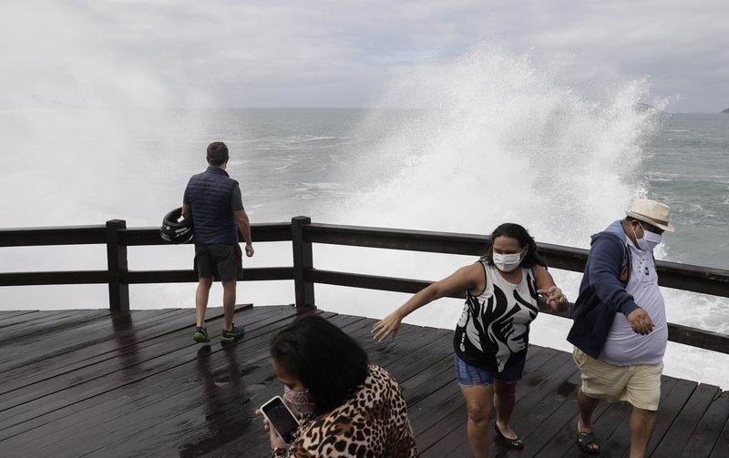 &copy; Reuters. Personas con mascarillas salen corriendo de la cubierta cuando las olas golpean las rocas en la playa de Leblon en medio del brote de coronavirus en Río de Janeiro, Brasil. 28 de mayo de 2020.