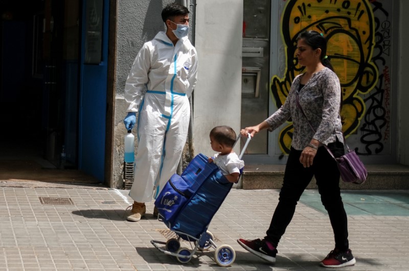 &copy; Reuters. FOTO DE ARCHIVO: Una mujer lleva a su hijo en un carrito de la compra delante de un voluntario que lleva una mascarilla y un traje de protección en el barrio del Raval, en Barcelona