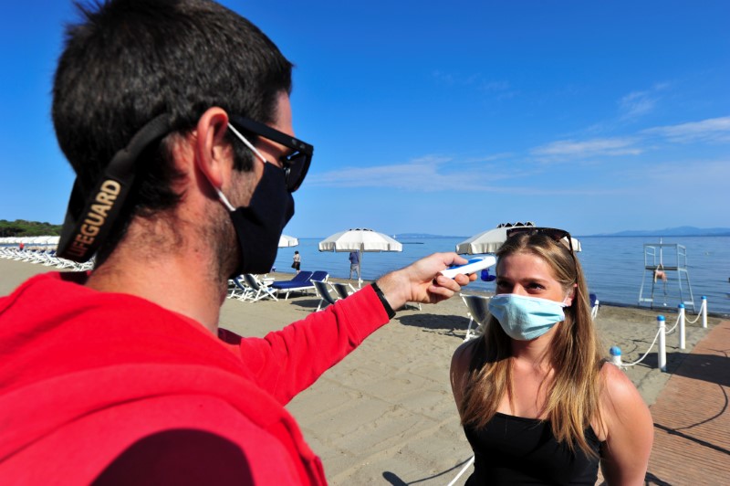 &copy; Reuters. Un salvavidas utilizando mascarilla toma la temperatura de una mujer en una playa recientemente abireta tras meses de cierre debido al brote de coronavirus, en Punta Hidalgo, Punta Ala, Italia