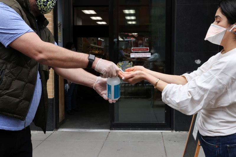 &copy; Reuters. A store worker offers hand sanitizer to shoppers on the sidewalk outside a grocery store in Washington