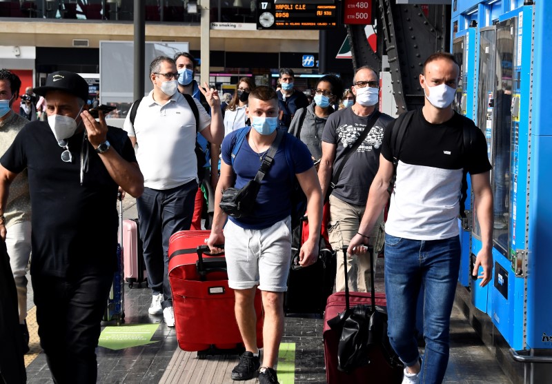 &copy; Reuters. Passageiros com máscara carregam malas em plataforma de trem em Milão
