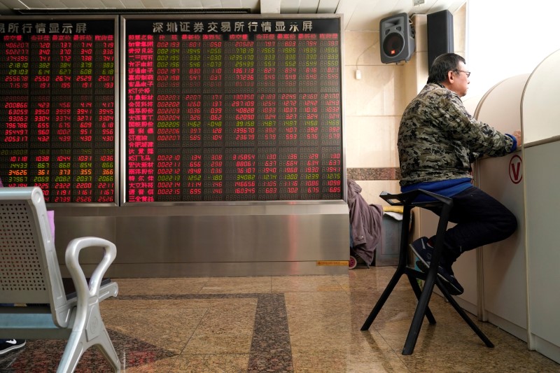 © Reuters. An investor sits next to a stock quotation board at a brokerage office in Beijing
