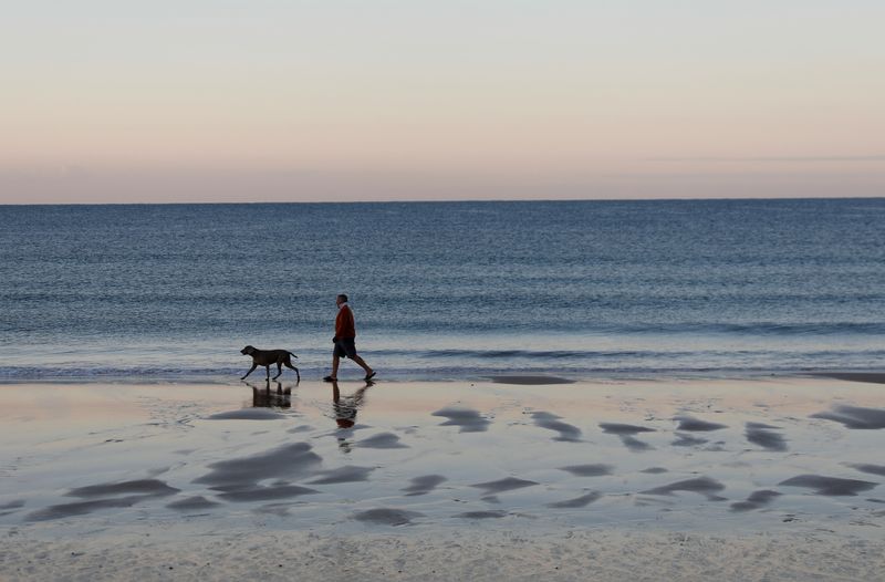 &copy; Reuters. A man walks his dog at the Praia da Luz beach