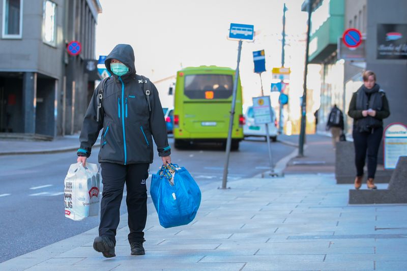 &copy; Reuters. Homem com máscara de proteção carrega sacola de compras em rua de Oslo