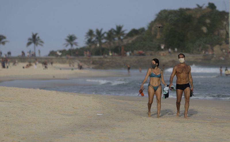 &copy; Reuters. Casal com máscara de proteção caminha na praia do Arpoador, no Rio de Janeiro