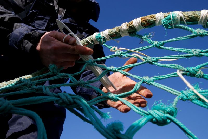 © Reuters. FILE PHOTO: A fisherman repairs a fishing net on the dock of the port in Boulogne-sur-Mer