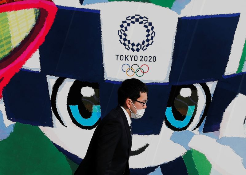 &copy; Reuters. A man wearing a protective mask walks past a large poster featuring Tokyo 2020 Olympic Games mascot Miraitowa amid the coronavirus disease (COVID-19) outbreak in Tokyo