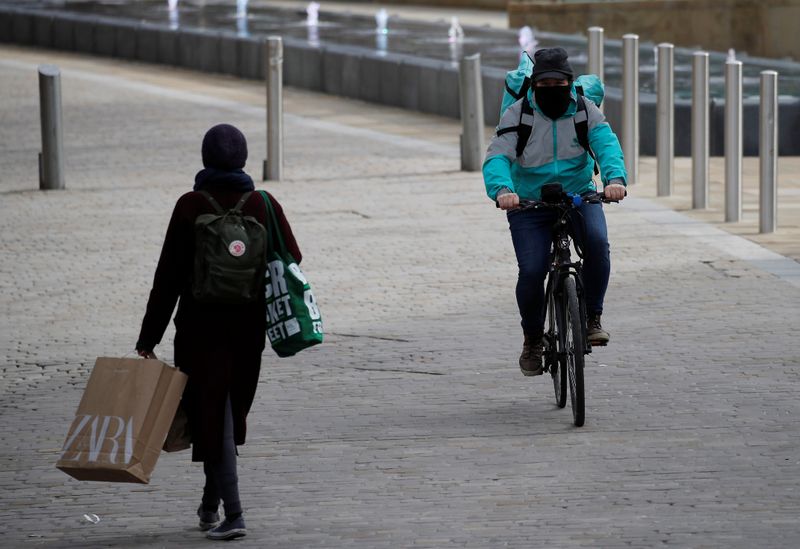 &copy; Reuters. A deliveroo rider with his face covered cycles past a woman carrying shopping bags amid the coronavirus outbreak in Manchester, Britain