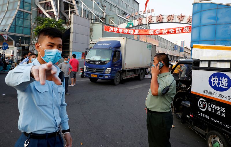 © Reuters. FOTO DE ARCHIVO: Los guardias de seguridad con máscaras faciales se enfrentan al mercado de mariscos Jingshen, que se cerró en Beijing después del descubrimiento de nuevas infecciones por coronavirus