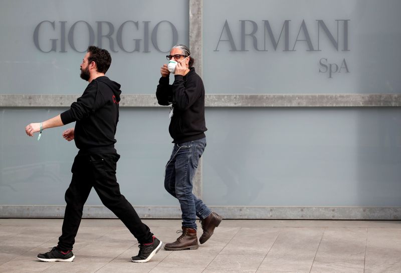 &copy; Reuters. Workers walk past the Giorgio Armani logo outside the theatre where the Italian designer said his Milan Fashion Week show would take place in Milan