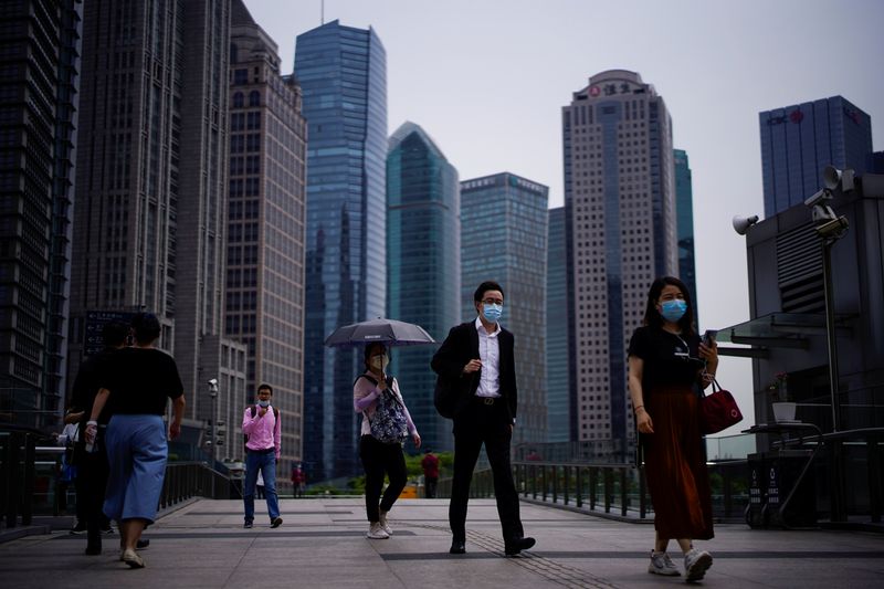 © Reuters. People wearing protective face masks walk past office buildings in Lujiazui financial district in Pudong, in Shanghai