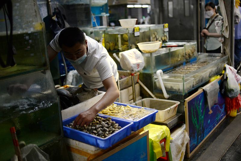 © Reuters. Vendor wearing a face mask prepares seafood at their stall inside the Yuegezhuang wholesale market, following new cases of coronavirus disease (COVID-19) infections in Beijing