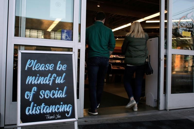 © Reuters. FILE PHOTO: Shoppers enter a grocery store near a sign requesting social distancing, following reports of coronavirus disease (COVID-19) cases in the area, in Seattle