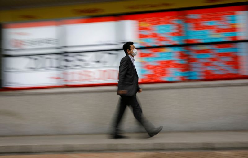 &copy; Reuters. A man wearing a protective face mask, following the coronavirus disease (COVID-19) outbreak, walks in front of a stock quotation board outside a brokerage in Tokyo