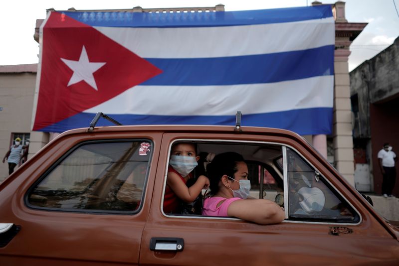 &copy; Reuters. FOTO DE ARCHIVO: Una familia en un coche pasando por delante de una bandera de Cuba en La Habana