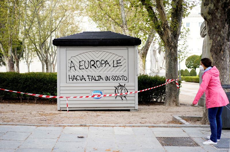 &copy; Reuters. FILE PHOTO: A woman wearing a protective mask stands next to a closed ice cream kiosk with a graffiti during lockdown