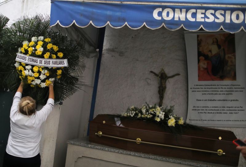 &copy; Reuters. Funcionária de cemitério coloca coroa de flores perto de caixão de vítima da Covid-19 no Rio de Janeiro