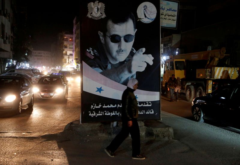 © Reuters. FILE PHOTO: A woman walks past a poster depicting Syria's President Bashar al-Assad in Damascus