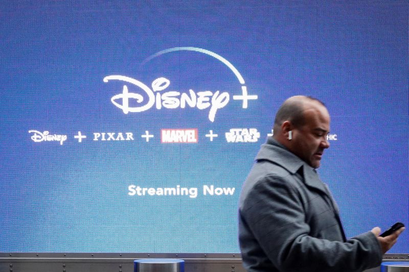 &copy; Reuters. A man looks at his phone as he passes by a screen advertising Walt Disney&apos;s streaming service Disney+ in New York