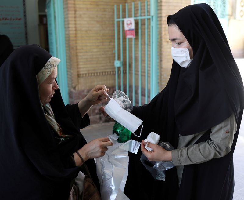 &copy; Reuters. Mulher entrega máscara para outra antes de orações de sexta-feira em mesquita do Irã