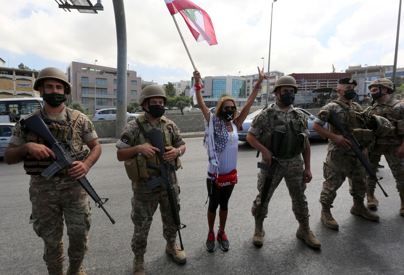 &copy; Reuters. Demonstrator raises Lebanese flag while standing between soldiers in Baabda