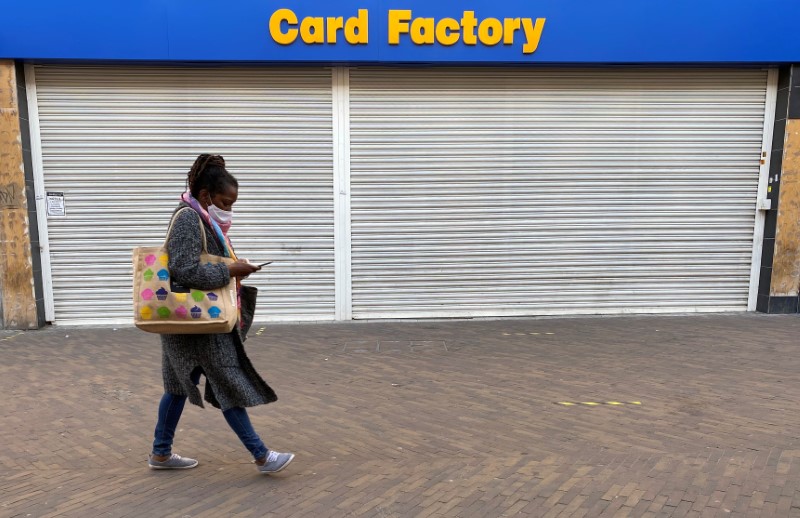 &copy; Reuters. A woman wearing a face mask walks past a shuttered branch of Card Factory in Hackney, London