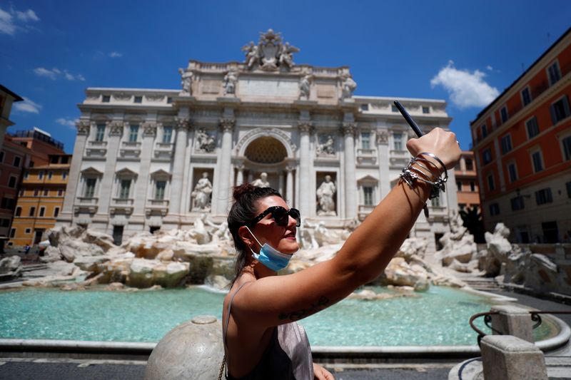 &copy; Reuters. Una donna si fa una foto davanti alla Fontana di Trevi a Roma, abbassando la maschera