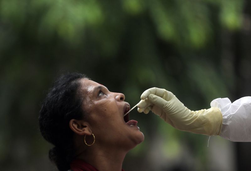 © Reuters. A health-worker wearing personal protective equipment (PPE) collects a sample using a swab from a woman during a check-up campaign for the coronavirus disease (COVID-19), at a residential society in Mumbai