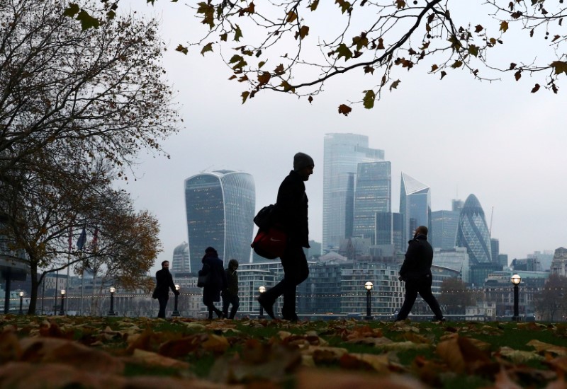 © Reuters. FILE PHOTO: People walk through autumnal leaves in front of the financial district in London