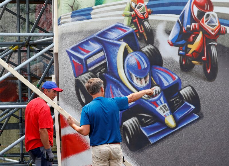 © Reuters. Workers stand in front of a poster next to the Formula One race track in Spielberg