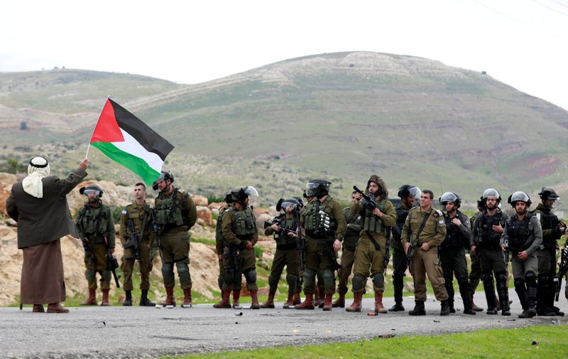 © Reuters. Un manifestante con una bandera palestina se manifiesta frente a fuerzas israelíes en una zona de Cisjordania.