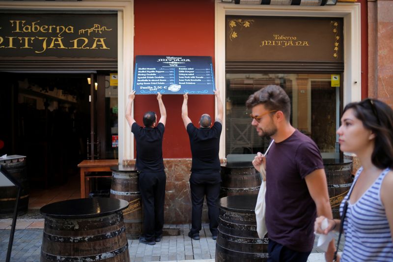 &copy; Reuters. FOTO DE ARCHIVO: Dos camareros colocan un cartel en el exteriro de un bar de Málaga