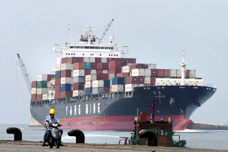 © Reuters. FILE PHOTO: People ride a motorcycle while a container ship passes by at Keelung port in northern Taiwan