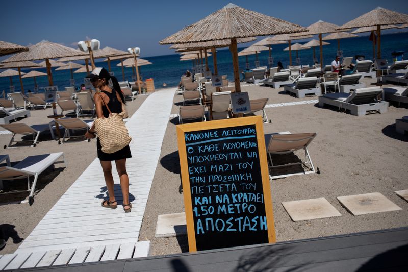 &copy; Reuters. A woman walks past an announcement calling for customers to maintain social distancing at a beach bar, following the coronavirus disease (COVID-19) outbreak, on the island of Kos
