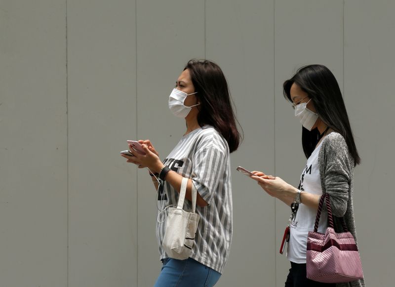 © Reuters. FILE PHOTO: Women wearing face masks use their mobile phones as haze shrouds Singapore's central business district