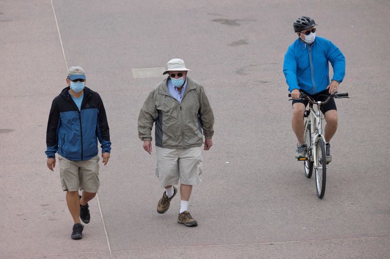 &copy; Reuters. Pessoas com máscaras de proteção caminham em calçadão de praia na Califórnia