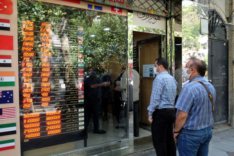 © Reuters. People wear protective face masks as they look at the electronic currency board at Ferdowsi square in Tehran