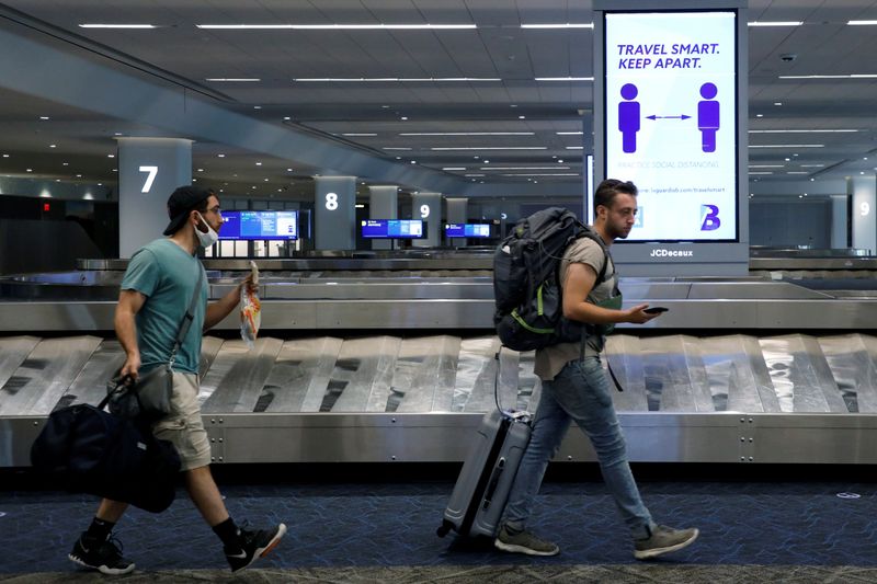 © Reuters. FILE PHOTO: Travelers pass a sign alerting them to distance at LaGuardia Airport, during the outbreak of the coronavirus disease (COVID-19), in New York