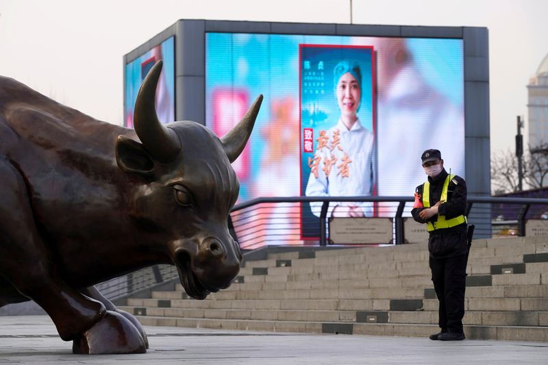 &copy; Reuters. FILE PHOTO: Security guard wearing a face mask stands near the Bund Financial Bull statue and a display showing an image of a medical worker on The Bund in Shanghai